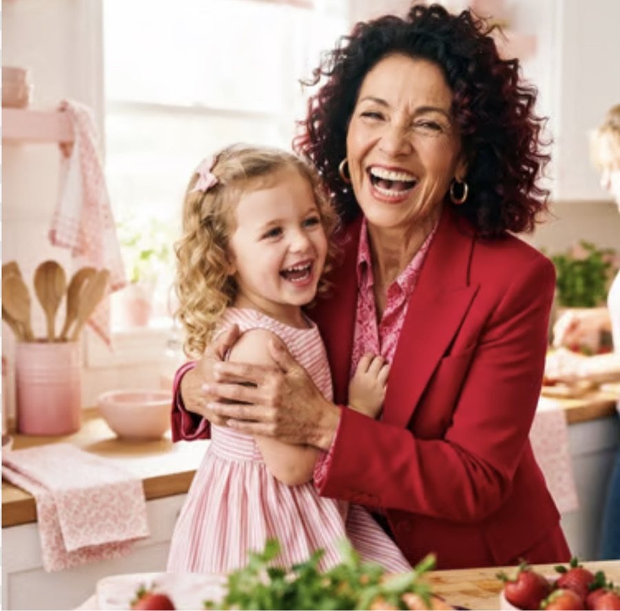 A woman in red laughing, a girl held against her
